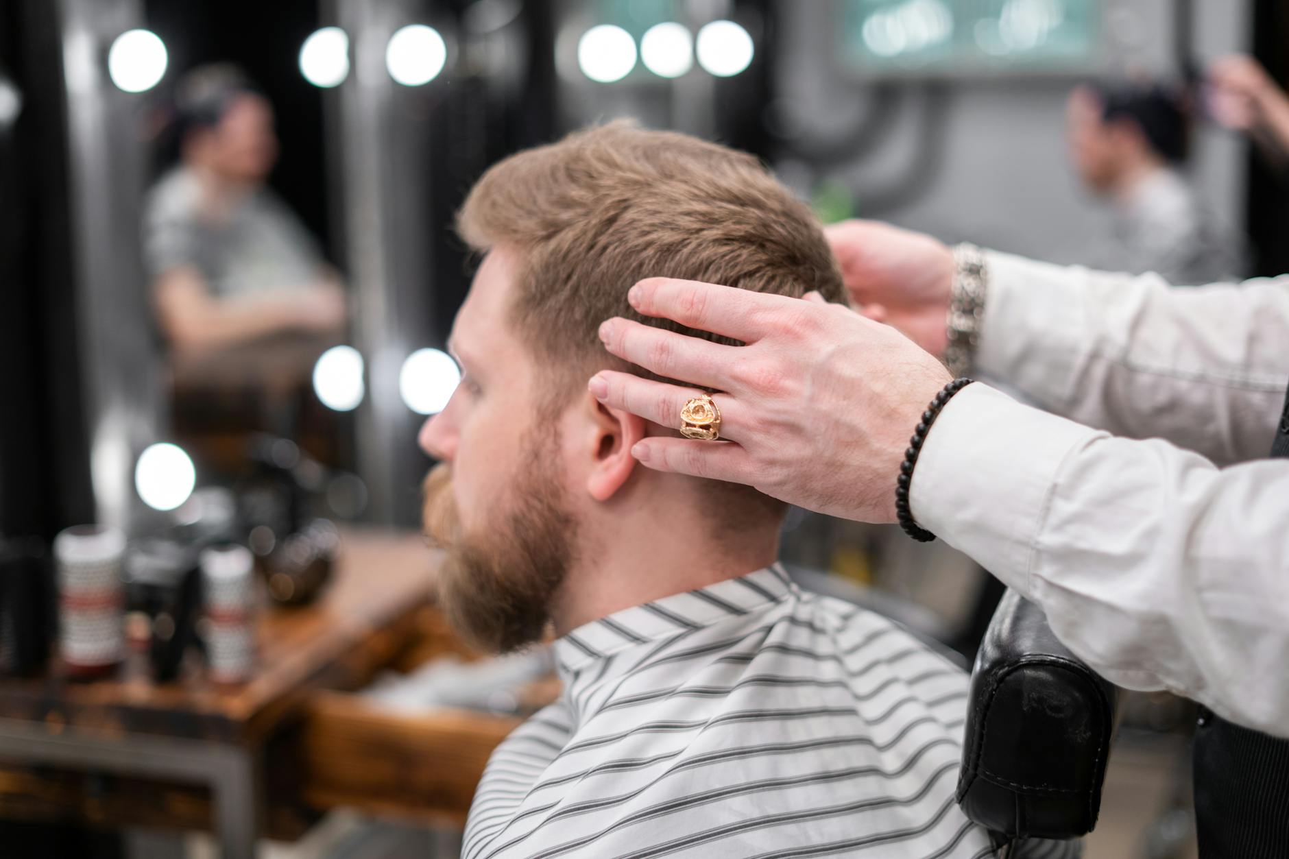 Barber styling a bearded man's hair in a modern barbershop setting.